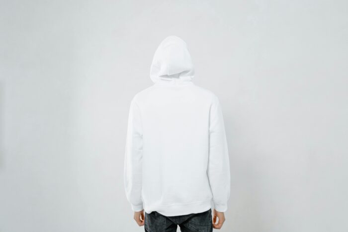 Person wearing a white hoodie facing away against a plain backdrop, offering blank space.